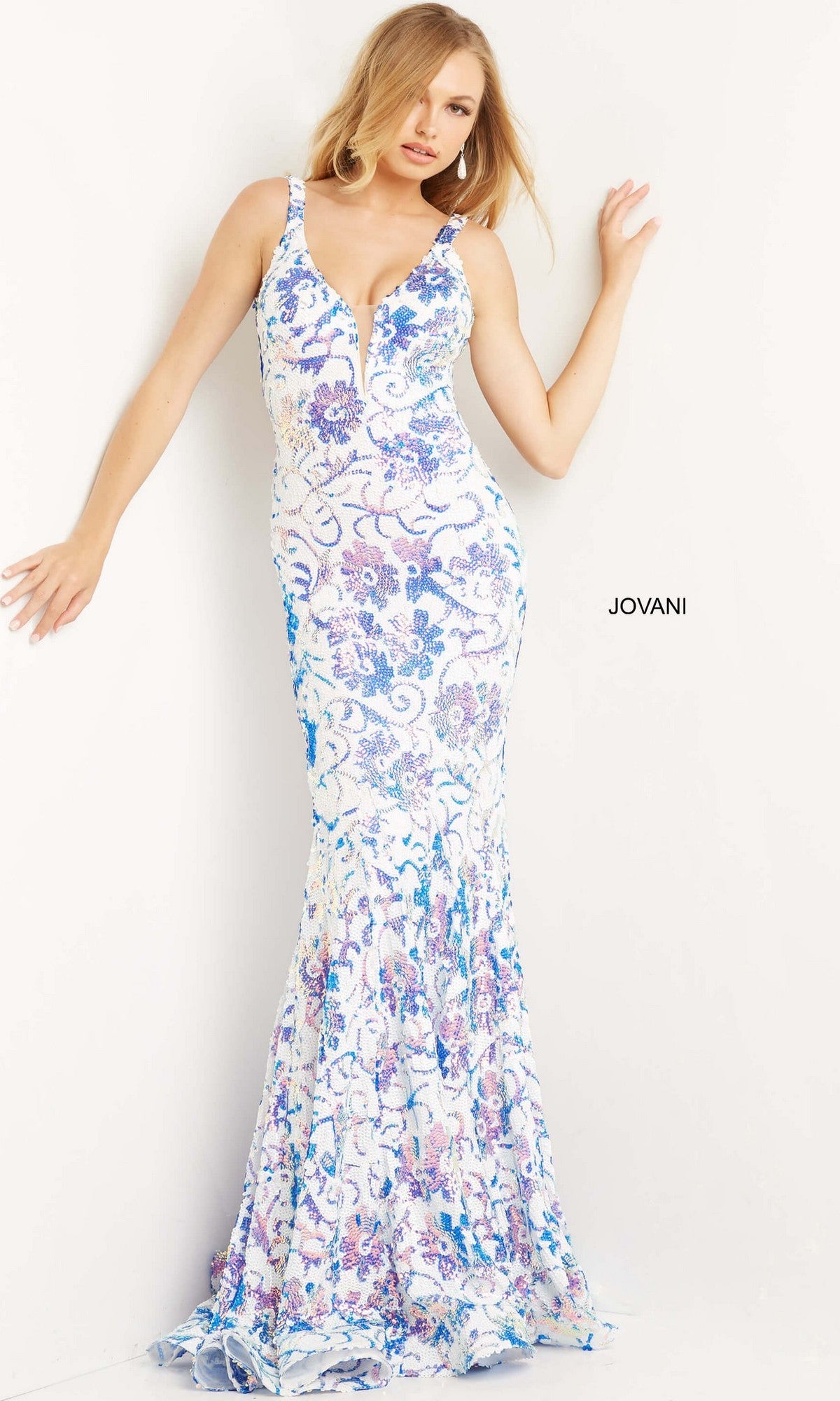 A woman poses against a white wall wearing the Jovani One-Shoulder Long Sequin Prom Dress 08256, a sleeveless floor-length designer gown with blue and purple floral patterns. The